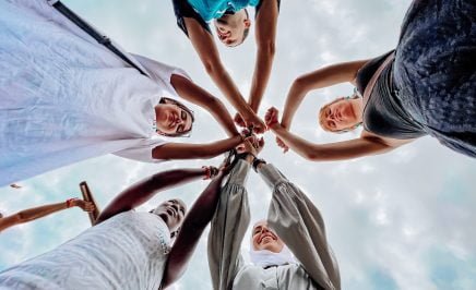 Five young people of diverse backgrounds join their closed fits in unity and solidarity in the centre of the group.
