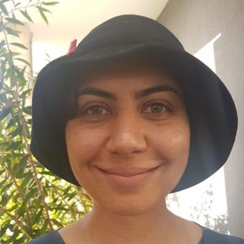 A portrait of Indigenous Rights activist, Caitlin Smith. She's smiling and wearing a black hat.