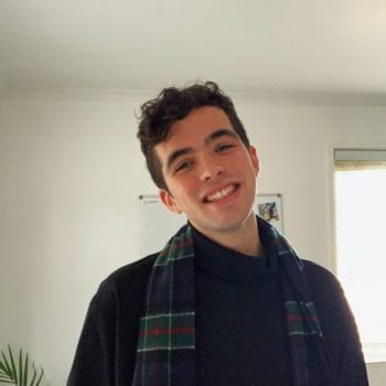 Portrait of Fin Spalding, LGBTIQ activist. Fin is smiling, wearing a black knitted top and green tartan scarf.