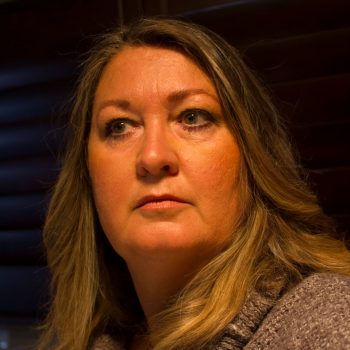 A portrait of Refugee Activist, Gabby Sutherland. She's looking away from the camera and wears a brown knitted top.