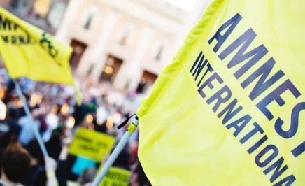 A close up of the Amnesty International flag someone is waving as part of a protest.