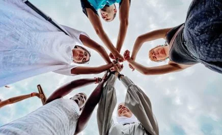 Five young people of diverse backgrounds join their closed fits in unity and solidarity in the centre of the group.