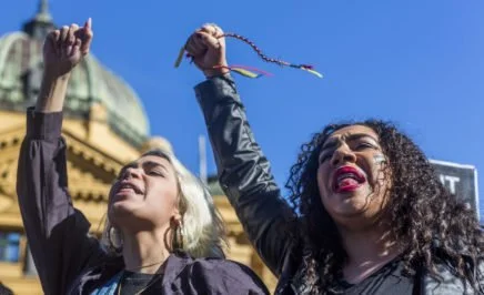 Two women with their fists in the air holding yellow, red and black ribbons.