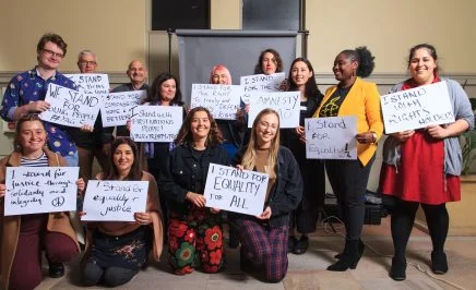 A group of people standing in a room hold up signs in support of various human rights